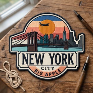 May include: Embroidered patch featuring a New York City design with the Brooklyn Bridge, skyline, and a setting sun. The patch includes the text "NEW YORK CITY BIG APPLE" in a stylized font. The patch is on a wooden surface.