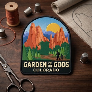May include: Embroidered patch featuring a scenic landscape of the Garden of the Gods in Colorado. The design includes orange rock formations, green trees, a yellow sun, and a path with two figures. Text reads "GARDEN OF THE GODS COLORADO".