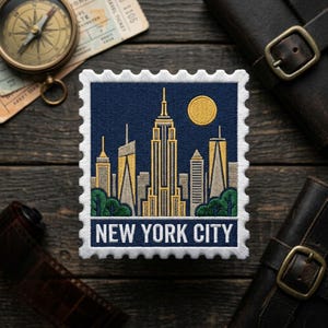 May include: Embroidered patch featuring a stylized New York City skyline with the text "NEW YORK CITY". The design includes the Empire State Building, other skyscrapers, a yellow sun, and green trees against a dark blue background. The patch has a white border.