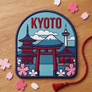 May include: Embroidered patch featuring a Kyoto, Japan design. The patch includes a red and blue pagoda, a mountain, a red torii gate, and the text "KYOTO" in red. Pink and white flower accents surround the patch, with a red tassel and cord.