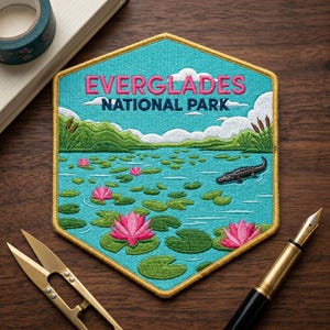 May include: A hexagonal embroidered patch featuring a turquoise water scene with pink water lilies, green lily pads, and a black alligator. The text EVERGLADES NATIONAL PARK is stitched in pink and dark blue against a backdrop of green hills and white clouds.
