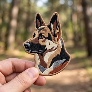 May include: An embroidered patch featuring the head of a German Shepherd dog. The design showcases detailed stitching in shades of black, tan, brown, and cream, capturing the canine's facial features, pointed ears, and distinct coat color patterns.