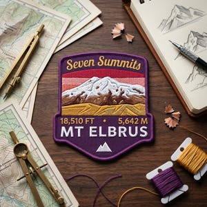 May include: An embroidered patch featuring a mountain landscape with a purple border, the text Seven Summits, and MT ELBRUS. The design includes a snow-capped peak, brown foothills, and yellow terrain, with the elevation 18,510 FT and 5,642 M printed below.
