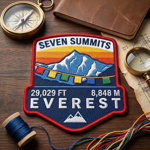 May include: A shield-shaped embroidered patch featuring a mountain peak, prayer flags, and the text SEVEN SUMMITS 29,029 FT 8,848 M EVEREST. The design includes a red border, a blue base, and a sunset-colored sky. The patch is displayed with a compass.