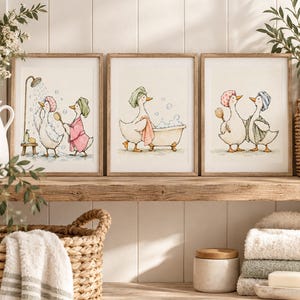 Op de afbeelding: Een set van drie ingelijste aquareldrukken met antropomorfe eenden in een badkamer. De illustraties tonen eenden met douchemutsen en handdoeken, die badborstels gebruiken en in een badkuip met zeepbellen baden.