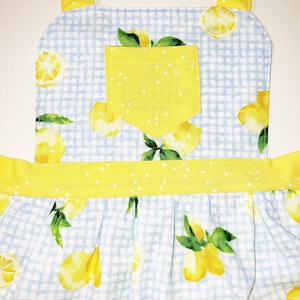 Puede incluir: Delantal con estampado de limones. El delantal presenta un patr&oacute;n de cuadros vichy azul claro con limones amarillos y hojas verdes. Tiene un bolsillo y correas amarillas. Ideal para cocinar o hornear.