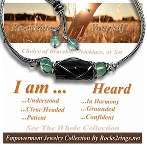 May include: A silver-toned necklace with a black tourmaline center stone, accented by green beads. The text reads "Re-create Yourself" and "I am Heard". The jewelry is part of the Empowerment Jewelry Collection.