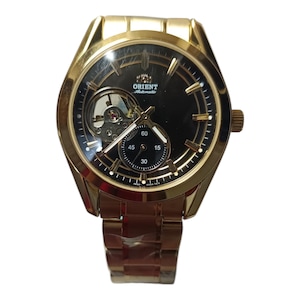 Może przedstawiać: Złoty zegarek Orient Automatic z czarną tarczą. Zegarek posiada widoczny mechanizm wewnętrzny i małą tarczę. Zegarek ma złotą bransoletę i koronkę po prawej stronie.