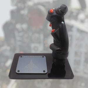 Peut inclure: Manche de commande noir avec des boutons rouges et une poignée texturée, monté sur une base noire. Une plaque argentée avec un dessin d'avion gravé est fixée à la base. Joystick pour simulation de vol.