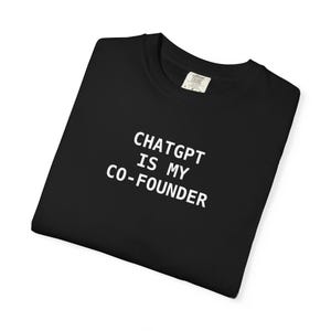 May include: Black t-shirt with the white text "CHATGPT IS MY CO-FOUNDER". The shirt is folded and has a tag on the collar.