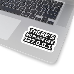 Peut inclure: Un autocollant blanc avec une bordure noire et le texte "THERE'S NO PLACE LIKE 127.0.0.1" en gras, sans empattement. L'autocollant est placé sur un ordinateur portable.