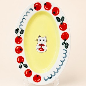 May include: Oval ceramic serving platter with a yellow center and white border. The border features a repeating blue wave pattern and red tomato illustrations. The center has a cartoon cat holding a tomato. A decorative piece for the kitchen.