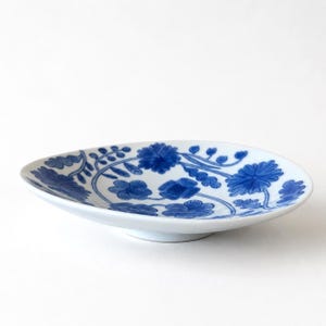 May include: White ceramic serving dish with a blue floral pattern. The dish has a shallow, oval shape and a slightly raised base. The blue floral design includes stylized flowers and vines, creating a decorative and elegant look.