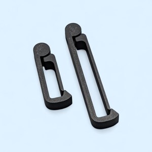 May include: Two dark gray, abstract-shaped objects. One is smaller and has a rounded top with a rectangular opening. The other is larger, with a similar design. The objects are on a light blue background.