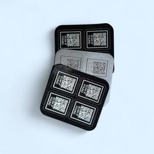 May include: A stack of square stickers with QR codes and the text "SCAN IF FOUND". The stickers are black and silver. Each sticker has four QR codes. The background is white.