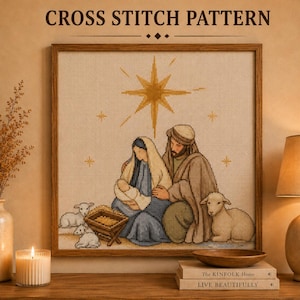 Può includere: Uno schema a punto croce intitolato CROSS STITCH PATTERN che raffigura una scena della natività con una stella dorata centrale, figure in vesti blu e marroni, un bambino in una mangiatoia e due agnelli bianchi in stile ricamo a griglia.