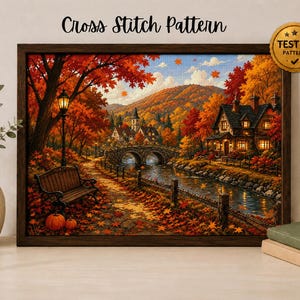 Puede incluir: Un patrón de punto de cruz enmarcado que muestra un paisaje otoñal con un puente de piedra, una cabaña, un banco de parque y follaje naranja y rojo vibrante. La imagen incluye el texto Cross Stitch Pattern y un sello dorado TESTED PATTERN.