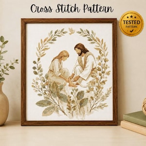Könnte beinhalten: Ein gerahmtes Kreuzstichmuster, das Jesus zeigt, wie er einer Person die Füße wäscht, umgeben von einem kreisförmigen Kranz aus grünen Blättern und einem kleinen Vogel oben. Der Text Cross Stitch Pattern und ein goldenes Tested Pattern Siegel sind sichtbar.