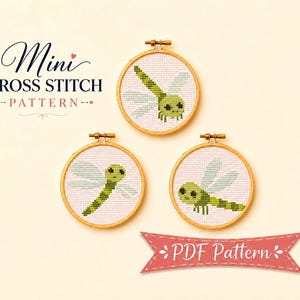 Op de afbeelding: Drie ronde houten borduurringen met kruissteekpatronen van groene libellen met lichtblauwe vleugels op witte stof. De tekst Mini CROSS STITCH PATTERN en PDF Pattern is zichtbaar in zwarte en rode schrijfletters en blokletters.