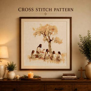 Puede incluir: Un patrón de punto de cruz enmarcado con una ilustración estilo acuarela de una figura sentada bajo un árbol con cuatro niños. El texto CROSS STITCH PATTERN aparece sobre el marco cuadrado, expuesto en una pared sobre una consola de madera.