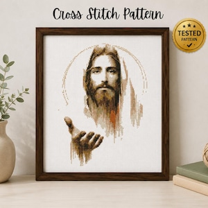 Puede incluir: Un patrón de punto de cruz enmarcado que muestra un retrato de Jesús con halo, en tonos marrones y bronceados sobre tela blanca. El texto "Cross Stitch Pattern" aparece arriba y un sello dorado "TESTED PATTERN" está en la esquina.