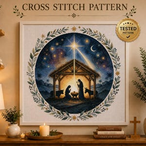 Puede incluir: Un patrón de punto de cruz con una escena de natividad circular con una estrella brillante, un establo y figuras en silueta. El diseño está enmarcado por una corona de hojas. El texto superior dice CROSS STITCH PATTERN y un sello dorado TESTED PATTERN.