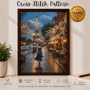 Puede incluir: Un patrón de punto de cruz enmarcado que muestra a una persona con un vestido azul caminando por un camino empedrado en París al atardecer. La Torre Eiffel está iluminada al fondo, con cerezos en flor y un café visibles cerca.