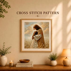 May include: A cross stitch pattern featuring a framed artwork of a figure in a tan robe embracing a person in a white robe within a field of flowers under a cloudy sky. The text CROSS STITCH PATTERN is printed in dark brown above the framed image.