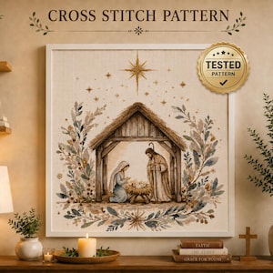 May include: A cross stitch pattern featuring a nativity scene with a stable, Mary, Joseph, and the infant Jesus under a star. The design is framed by botanical elements and includes the text CROSS STITCH PATTERN and a gold TESTED PATTERN seal.