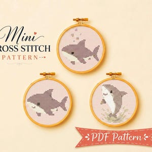 May include: Three circular wooden embroidery hoops containing cross stitch patterns of grey and white sharks on a light background. The text Mini CROSS STITCH PATTERN appears on the left, and a red banner with PDF Pattern is at the bottom.