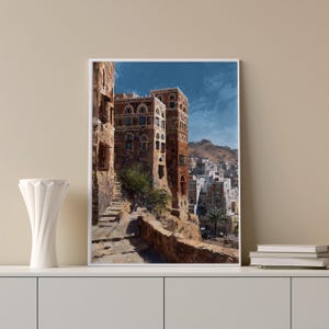 May include: An art print of a Middle Eastern cityscape. The painting depicts tall, brown buildings with arched windows and a winding street. The sky is a vibrant blue, and the overall scene evokes a sense of history and culture.