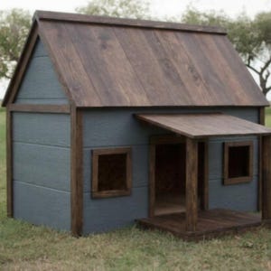 Puede incluir: Una caseta para perros de madera, con techo y molduras marrón oscuro y paredes azul grisáceo. La casa tiene un pequeño porche y dos ventanas. Está situada sobre un césped con árboles al fondo.