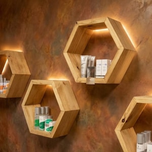 May include: Wooden hexagon-shaped shelves with built-in lighting, mounted on a textured brown wall. The shelves display various cosmetic products, creating a modern and stylish storage solution.