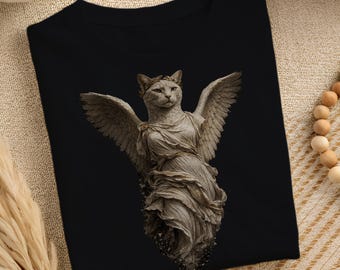 Könnte beinhalten: Ein schwarzes T-Shirt mit einem Grafikdruck einer steinfarbenen Katze mit großen gefiederten Flügeln, die ein drapiertes Gewand und einen Lorbeerkranz auf dem Kopf trägt. Die Katze hat einen ernsten Gesichtsausdruck im Stil einer Statue.