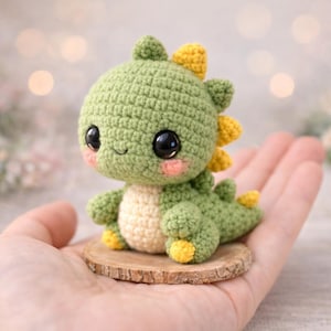 Könnte beinhalten: Ein handgehäkeltes Dinosaurier-Amigurumi in Grün-, Gelb- und Cremetönen, mit großen schwarzen Augen und rosigen Wangen. Der Dinosaurier sitzt auf einer kleinen Holzscheibe.