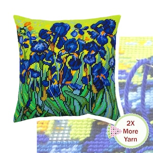 May include: A square needlepoint pillow featuring a vibrant cross-stitch pattern of blue irises against a bright yellow and green background. A circular badge on the lower right corner displays the text 2X More Yarn with a needle and blue yarn.