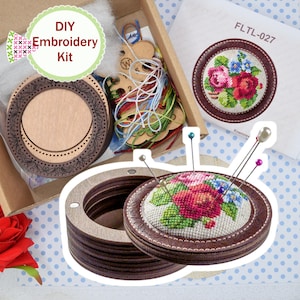 May include: DIY embroidery kit featuring a wooden embroidery hoop and a floral cross-stitch design. The kit includes a pin cushion with colorful pins, embroidery floss, and the text "DIY Embroidery Kit". The design includes red, pink, and blue flowers.