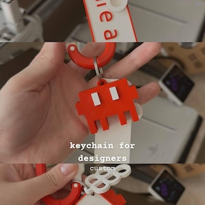 May include: A red and white keychain featuring a pixelated alien character, a circular ring, and a rectangular tag with the text share a file. The design includes a white layered element with circular cutouts attached to a red plastic carabiner clip.