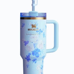 May include: A white ceramic mug with a black handle and the text "But First, Coffee" in a bold, black font. The mug is set against a blurred background, suggesting a cosy setting.