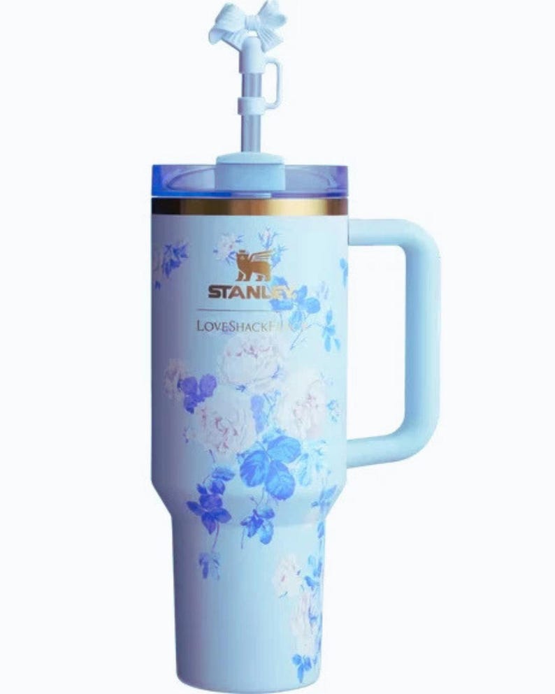 May include: A white ceramic mug with a black handle and the text "But First, Coffee" in a bold, black font. The mug is set against a blurred background, suggesting a cosy setting.