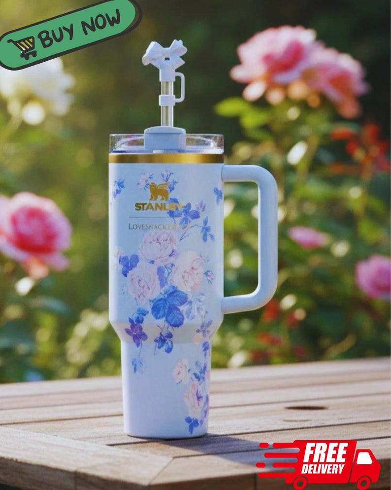 May include: A light blue insulated travel mug with a handle, decorated with a floral design in pink and blue. It includes a straw and a decorative top. The mug has the brand name "STANLEY" and the text "LOVESHACKE".