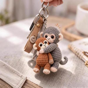 May include: A handmade crochet keychain featuring two hugging monkey figures. One monkey is brown, the other is gray. The keychain includes a leather strap with keys and a smiley face charm.
