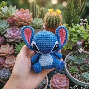 May include: A handmade blue crochet Stitch doll with pink inner ears and black eyes. The plush toy is held in front of a background of various succulents and cacti in pots, with soft sunlight in the background.