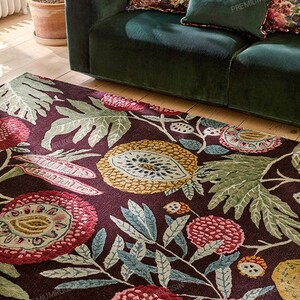 May include: A dark burgundy area rug with a floral pattern featuring large, stylized flowers in shades of red, yellow, and blue-green. The rug is placed on a hardwood floor, with a green velvet sofa in the background.