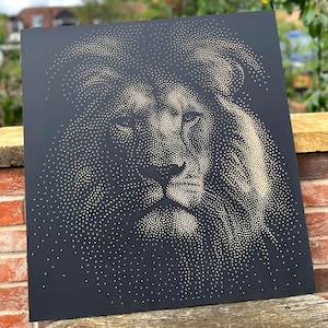 May include: A square black wall art panel featuring a lion portrait created with a stippled dot pattern in a light gold or beige color. The dots vary in density to form the facial features, eyes, and mane of the lion against the dark background.
