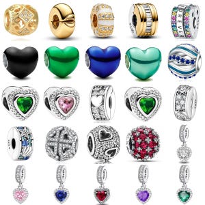 May include: A collection of various charms and pendants, including heart-shaped, round, and cylindrical designs. The charms feature a variety of colors, including gold, silver, black, green, blue, and pink. Some charms are adorned with gemstones and intricate patterns.