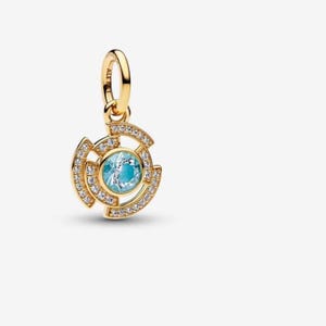 May include: A gold-plated charm featuring a central round light blue stone surrounded by a geometric frame set with clear cubic zirconia stones. The charm includes a small circular bail at the top with the engraved text ALE MET.