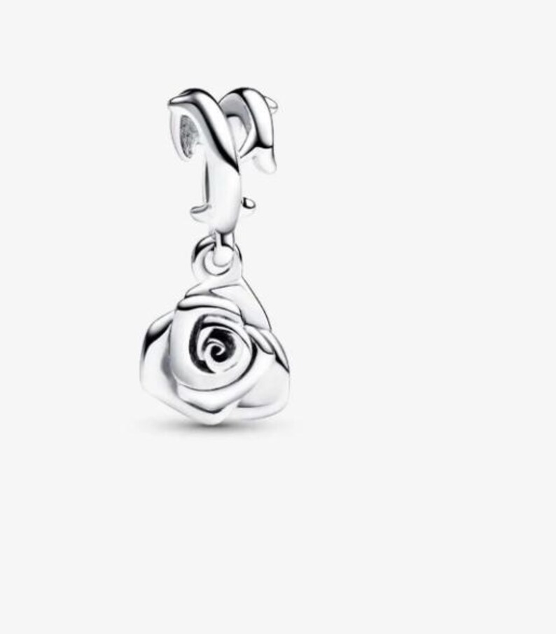 May include: A polished silver charm featuring a dangling rose pendant. The charm has a curved, smooth bail at the top designed for attachment to a bracelet or necklace chain, with a detailed, layered rose flower shape hanging below it.