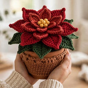 May include: A crocheted poinsettia plant with deep red petals and dark green leaves, featuring a cluster of small yellow centers. The plant is housed in a terracotta pot covered by a textured, light brown crocheted cozy.