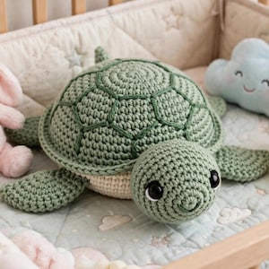 May include: A crocheted sea turtle plush toy with a sage green shell and a cream-colored underside, featuring large black safety eyes. It is positioned between a light pink plush rabbit, a light blue plush cloud, and a yellow plush duck.